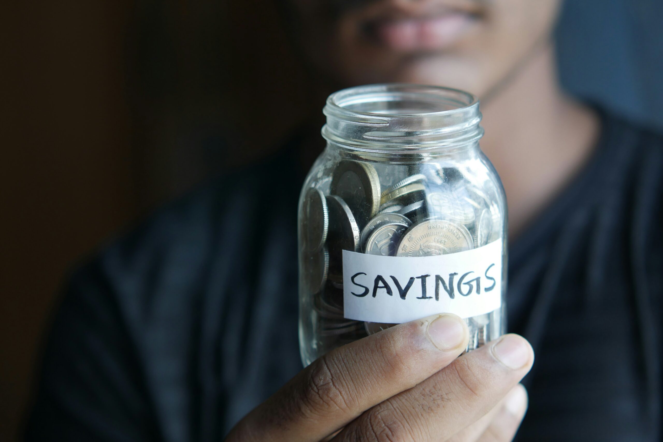 Person holding a glass jar labeled savings with coins inside
